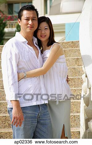 Couple standing, embracing, looking at camera View Large Photo Image Stock Photograph - Couple standing, embracing, looking at camera . Fotosearch