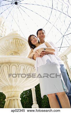 Couple standing, embracing, looking at down camera View Large Photo Image Stock Photography - Couple standing, embracing, looking at down camera . Fotosearch