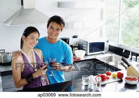 Couple standing in kitchen, holding wine glasses, looking at camera View Large Photo Image Stock Photo - Couple standing in kitchen, holding wine glasses, looking at camera . Fotosearch