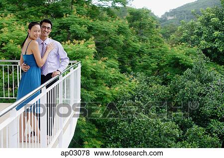 Couple standing on balcony, embracing, looking at camera View Large Photo Image Stock Photo - Couple standing on balcony, embracing, looking at camera . Fotosearch