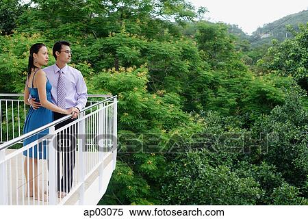 Stock Photography - Couple standing on balcony, looking away . Fotosearch