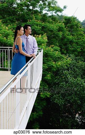 Stock Photograph - Couple standing on balcony, side view. Fotosearch