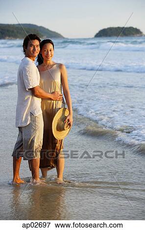 Couple standing on beach, ankle deep in water, looking at camera View Large Photo Image Stock Photo - Couple standing on beach, ankle deep in water, looking at camera . Fotosearch