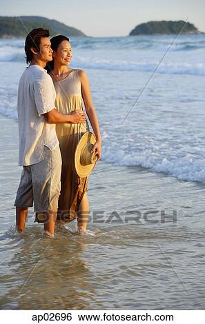 Couple standing on beach, ankle deep in water View Large Photo Image Stock Photograph - Couple standing on beach, ankle deep in water . Fotosearch