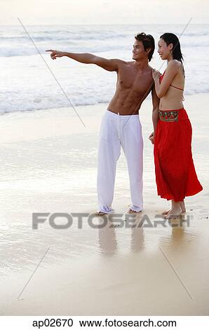Couple standing on beach, holding hands, man pointing View Large Photo Image Stock Image - Couple standing on beach, holding hands, man pointing . Fotosearch