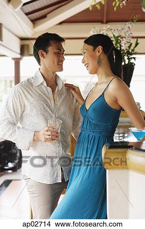 Picture - Couple standing side by side, holding drinks, looking away . Fotosearch