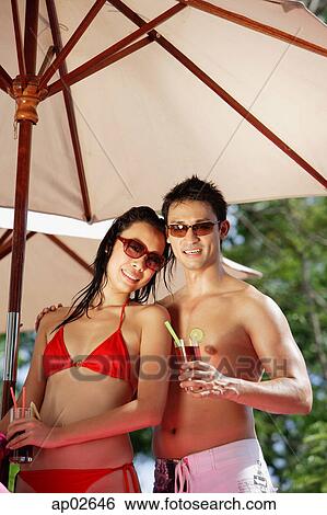 Couple standing under umbrella, holding drinks View Large Photo Image Stock Photograph - Couple standing under umbrella, holding drinks . Fotosearch