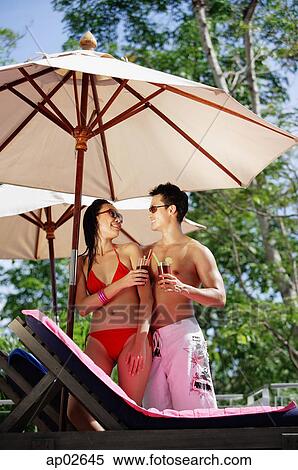 Stock Photography - Couple standing under umbrella, looking at each other, holding drink . Fotosearch