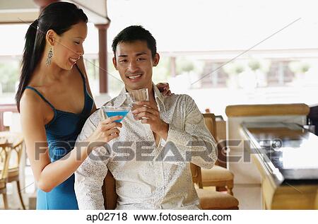 Stock Photo - Couple toasting with drinks, man looking at camera . Fotosearch