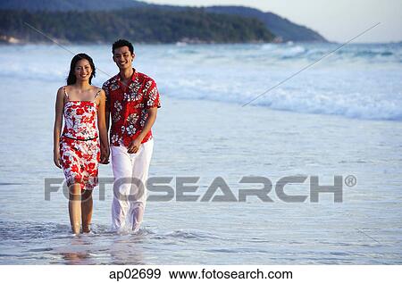 Couple walking on beach, ankle deep in water, holding hands, smiling at camera View Large Photo Image Stock Photo - Couple walking on beach, ankle deep in water, holding hands, smiling at camera . Fotosearch