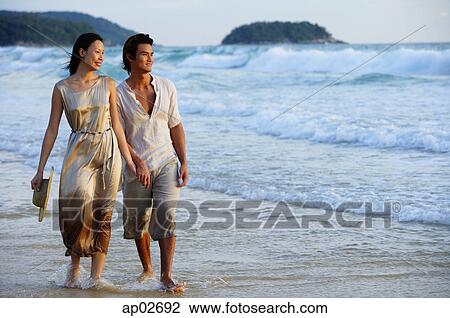 Stock Image - Couple walking on beach, looking away . Fotosearch