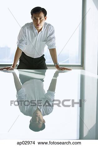 Executive leaning on table, looking at camera View Large Photo Image Picture - Executive leaning on table, looking at camera . Fotosearch