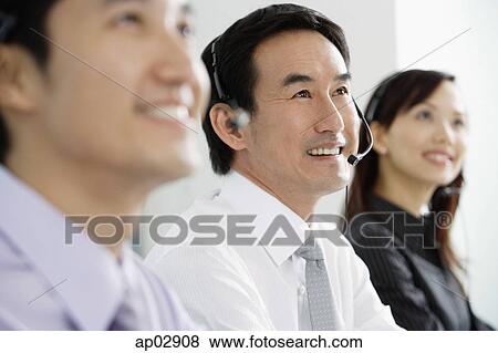 Executives in a row, wearing headsets, looking away, smiling View Large Photo Image Stock Photo - Executives in a row, wearing headsets, looking away, smiling . Fotosearch