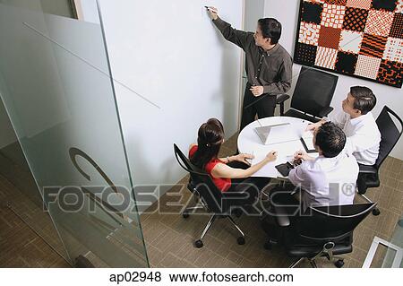 Executives in meeting room, one writing on whiteboard View Large Photo Image Stock Photo - Executives in meeting room, one writing on whiteboard . Fotosearch