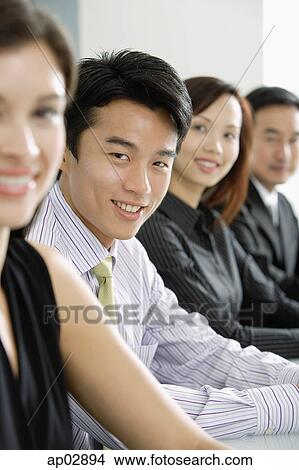 Picture - Executives sitting in a row, looking at camera, smiling, portrait . Fotosearch