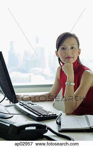 Female executive sitting at office desk, looking at camera View Large Photo Image Stock Photo - Female executive sitting at office desk, looking at camera . Fotosearch