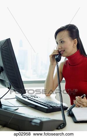 Female executive sitting at office desk, using telephone View Large Photo Image Stock Photo - Female executive sitting at office desk, using telephone. Fotosearch