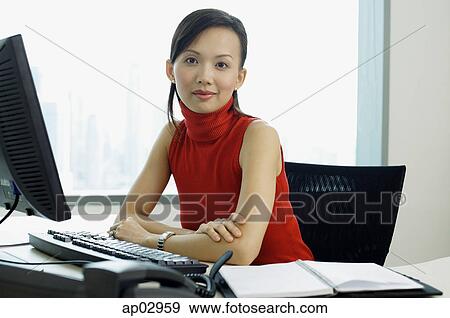 Stock Photo - Female executive sitting at office desk, portrait. Fotosearch