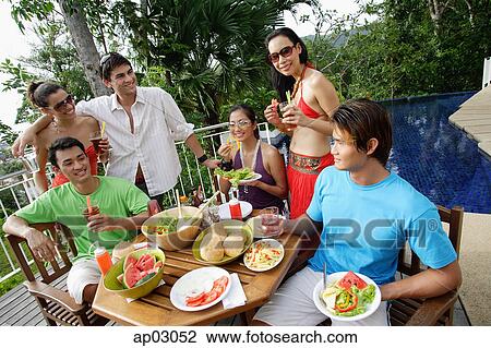 Stock Image - Group of young adults having a meal on patio. Fotosearch