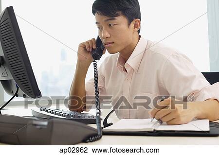 Male executive sitting at office desk, using telephone View Large Photo Image Stock Image - Male executive sitting at office desk, using telephone . Fotosearch