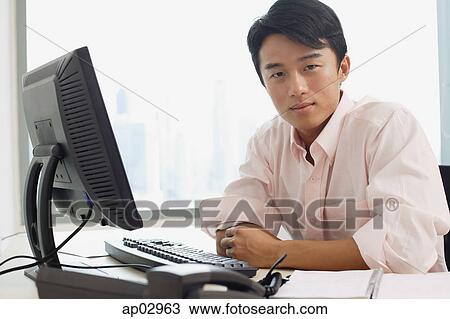 Male executive sitting at office desk, looking at camera View Large Photo Image Stock Image - Male executive sitting at office desk, looking at camera. Fotosearch