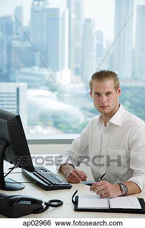 Stock Photograph - Male executive sitting at office desk, looking at camera . Fotosearch