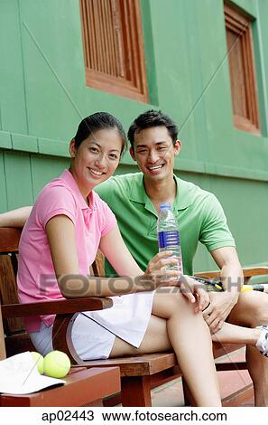 Stock Image - Man and woman sitting on bench, smiling at camera, woman with water bottle . Fotosearch