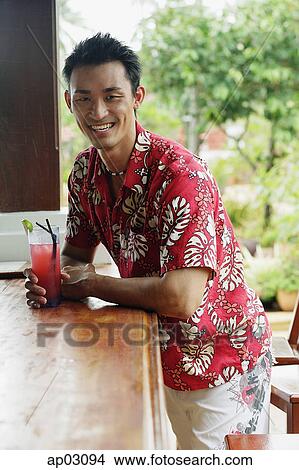 Picture - Man at beach bar, with drink, smiling at camera . Fotosearch
