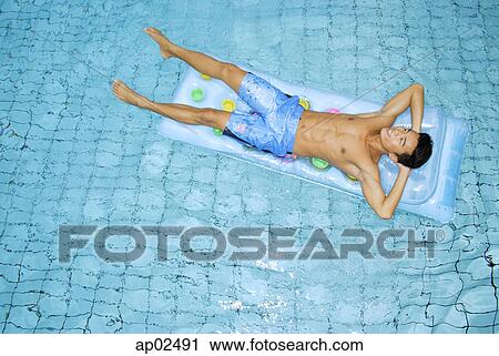 Stock Image - Man lying on pool raft, hands behind head . Fotosearch