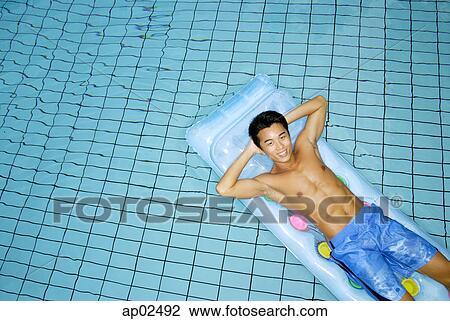 Stock Image - Man lying on pool raft, hands behind head, looking at camera . Fotosearch