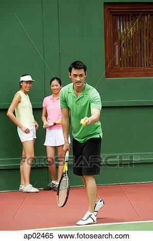 Stock Photography - Man serving a game of tennis with two women watching . Fotosearch