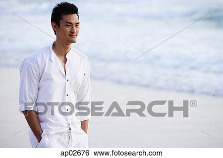 Stock Photograph - Man standing on beach, hands in pocket. Fotosearch