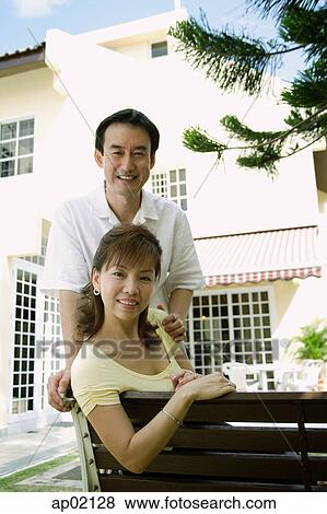 Mature couple looking at camera smiling, husband standing behind wife View Large Photo Image Stock Photo - Mature couple looking at camera smiling, husband standing behind wife . Fotosearch