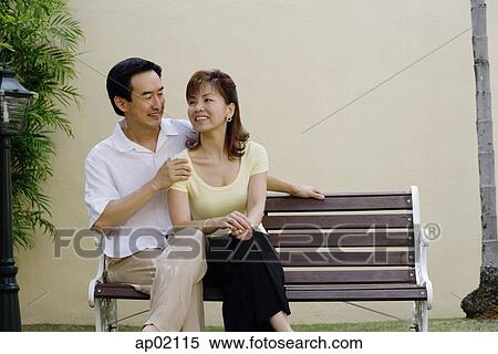 Stock Photography - Mature couple sitting on bench, man with arms around woman . Fotosearch