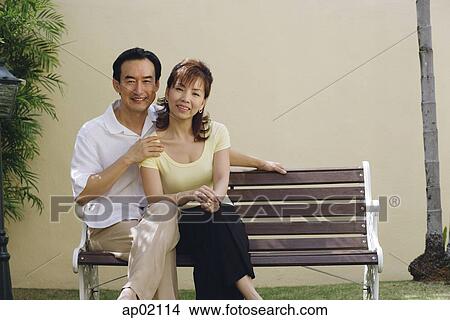 Picture - Mature couple sitting on bench, smiling at camera . Fotosearch