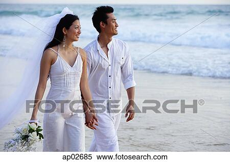 Stock Photography - Newlyweds walking on beach, holding hands, looking away . Fotosearch