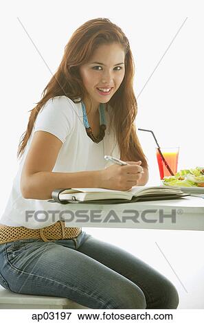 One woman sitting at table, writing in notebook, smiling at camera View Large Photo Image Stock Photo - One woman sitting at table, writing in notebook, smiling at camera. Fotosearch
