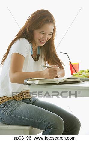 One woman sitting at table, writing in notebook, smiling View Large Photo Image Stock Photograph - One woman sitting at table, writing in notebook, smiling. Fotosearch