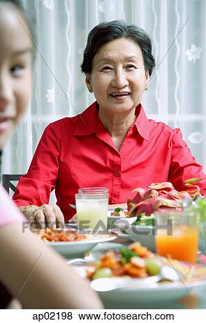 Senior adult at dining table, smiling at camera, granddaughter in the foreground View Large Photo Image Stock Photo - Senior adult at dining table, smiling at camera, granddaughter in the foreground . Fotosearch