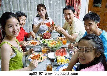 Stock Photo - Three generation family around dining table, looking at camera . Fotosearch