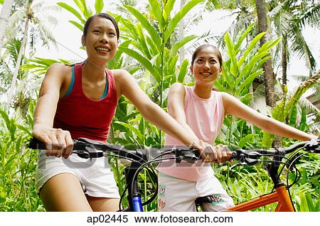 Two girls riding bikes through a park, smiling View Large Photo Image Stock Photography - Two girls riding bikes through a park, smiling . Fotosearch