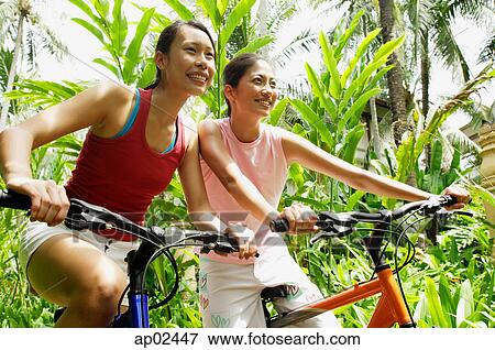 Two girls smiling and riding bikes through a park View Large Photo Image Stock Photo - Two girls smiling and riding bikes through a park . Fotosearch