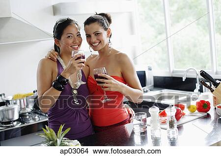 Picture - Two women in kitchen, drinks in hand, smiling at camera . Fotosearch