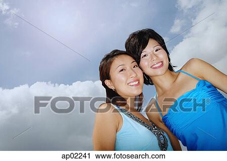 Two women standing cheek to cheek, smiling at camera, low angle view View Large Photo Image Stock Image - Two women standing cheek to cheek, smiling at camera, low angle view . Fotosearch
