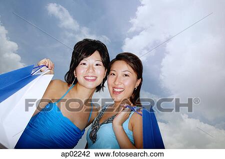Two women standing cheek to cheek, carrying shopping bags, low angle view View Large Photo Image Stock Image - Two women standing cheek to cheek, carrying shopping bags, low angle view . Fotosearch