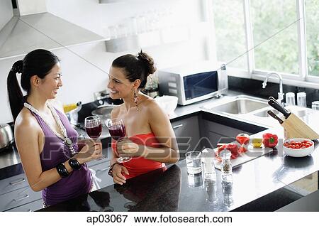 Two women standing in kitchen, holding wine glasses View Large Photo Image Stock Photo - Two women standing in kitchen, holding wine glasses . Fotosearch