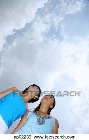 Two women standing side by side, looking away, low angle view View Large Photo Image Stock Photo - Two women standing side by side, looking away, low angle view . Fotosearch