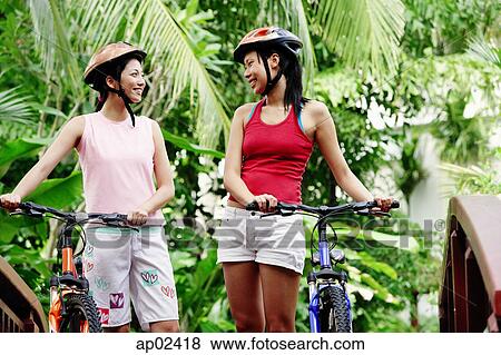 Two women standing with bicycles, smiling at each other View Large Photo Image Stock Photo - Two women standing with bicycles, smiling at each other. Fotosearch