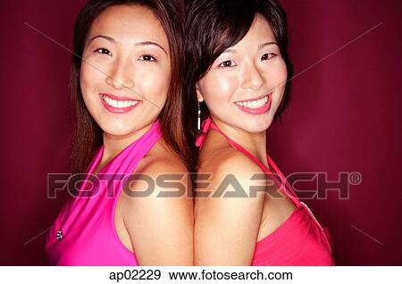 Two young women standing back to back, smiling at camera View Large Photo Image Stock Photo - Two young women standing back to back, smiling at camera . Fotosearch