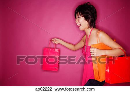 Stock Image - Woman carrying shopping bags, side view. Fotosearch
